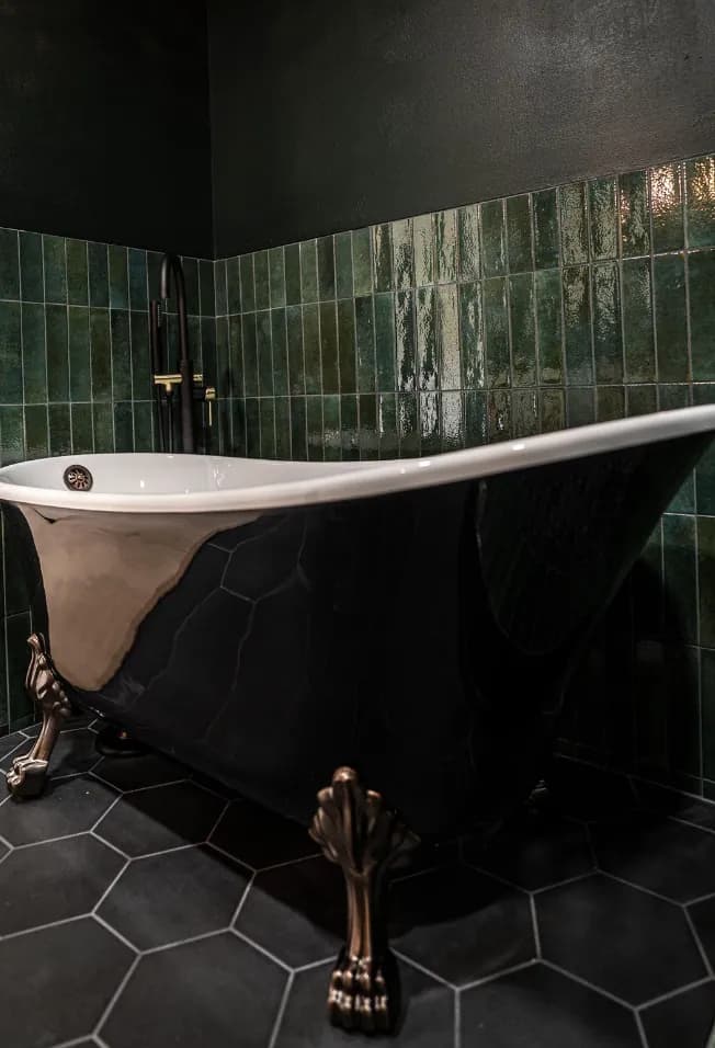 Clawfoot tub close-up on black hex floor tile with green tile wall