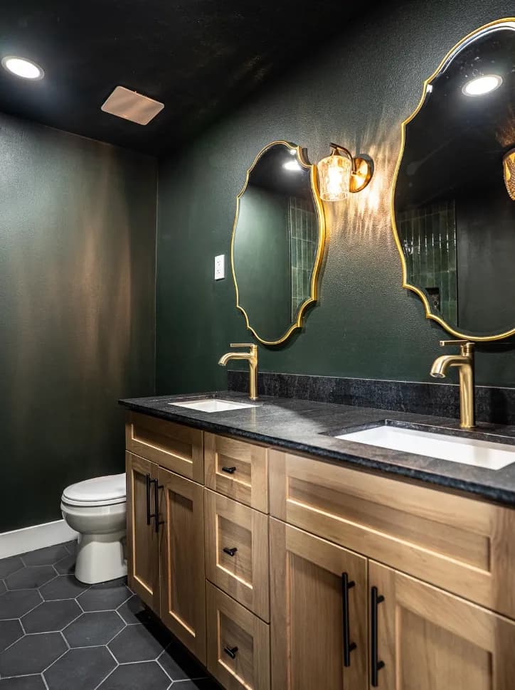 White-oak double vanity, black counter, gold scalloped mirrors and sconces, dark green walls
