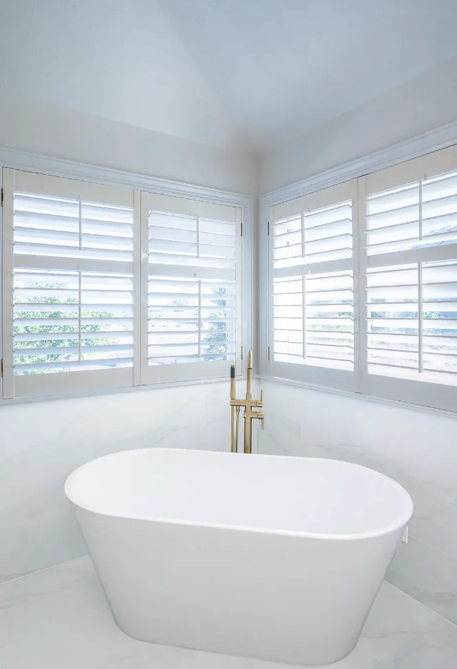 Freestanding white tub with brass floor-mount filler under shuttered windows