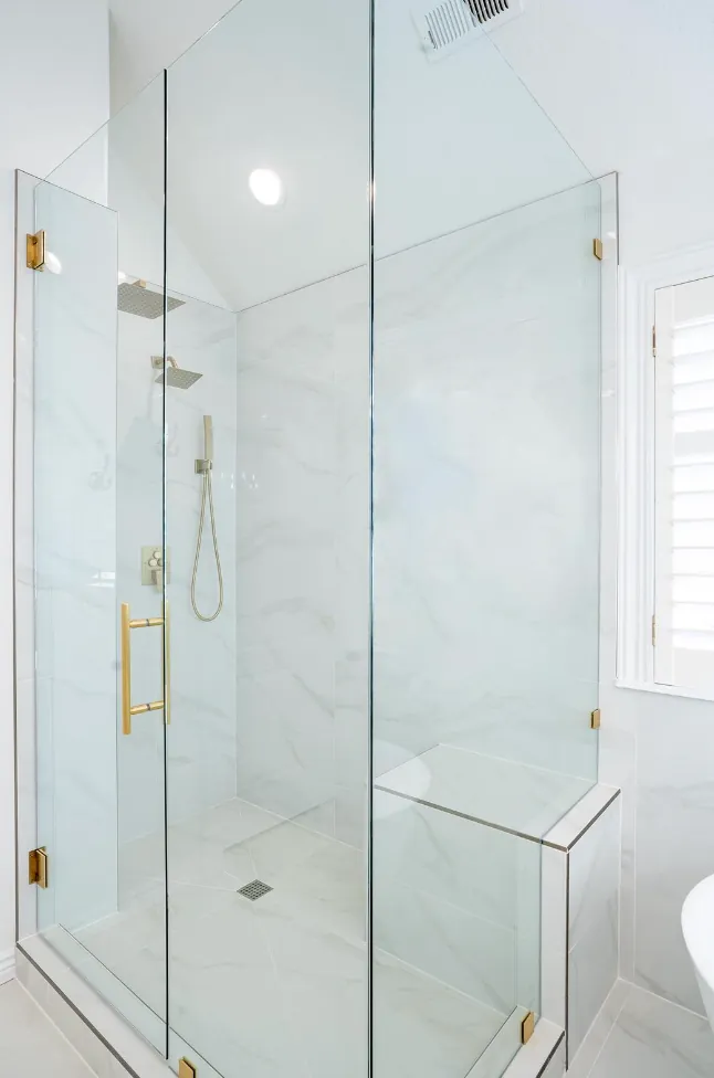 Frameless glass shower with marble-look tile, bench and gold fixtures