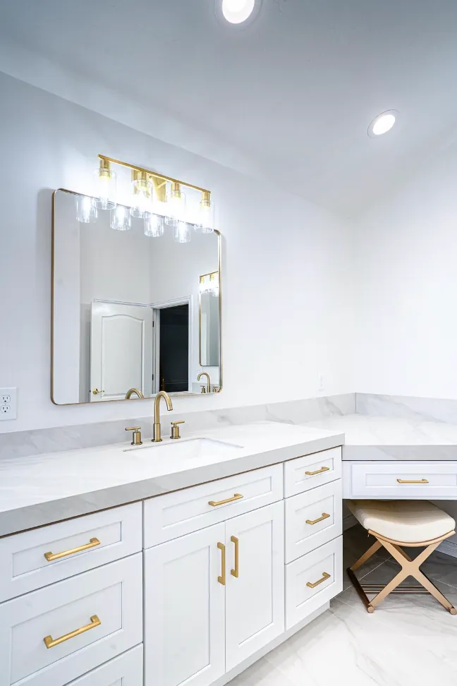 White vanity with gold pulls, marble-look counter, makeup station with stool