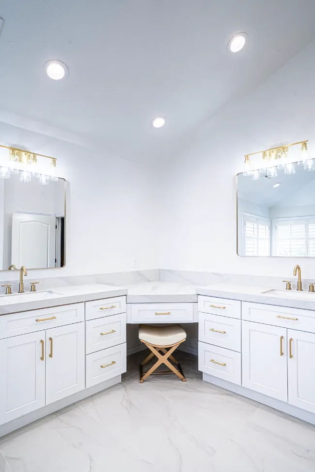 Corner his-and-hers white vanities with makeup station, gold light bars