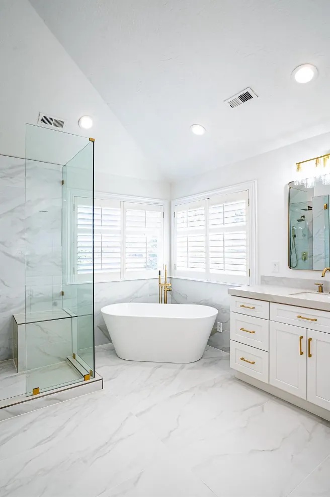 Primary bath wide view: glass shower, freestanding tub, white vanity, vaulted ceiling