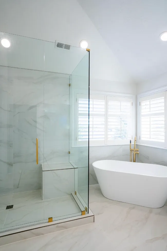 Glass shower with bench and freestanding tub beyond