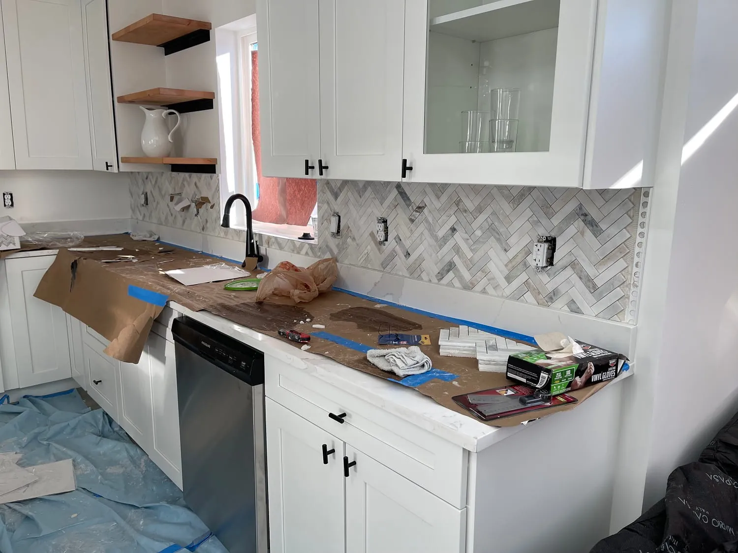 Herringbone marble backsplash being installed, counters protected with paper