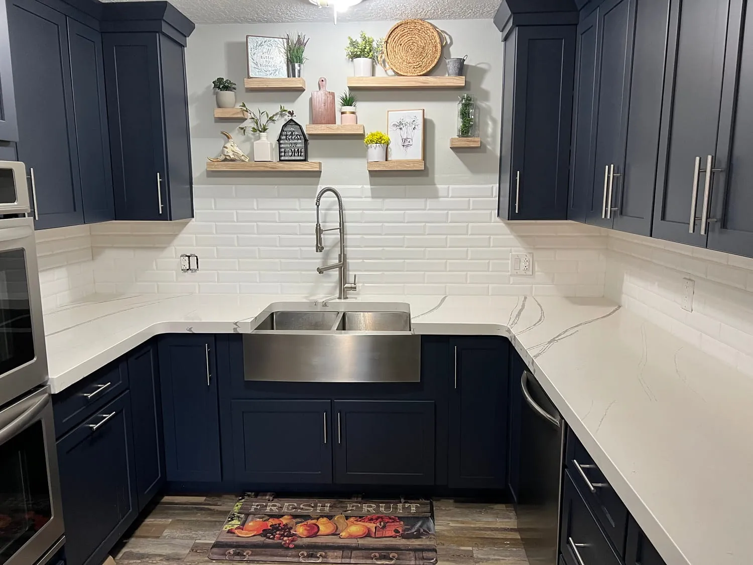 Navy-blue upper/lower cabinets, white quartz, stainless apron-front sink, open wood shelves