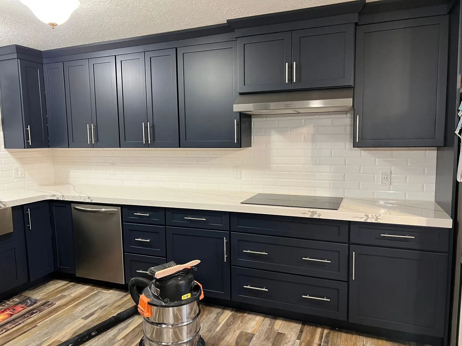 Navy-blue shaker cabinets with white quartz and white subway tile, shop-vac on floor
