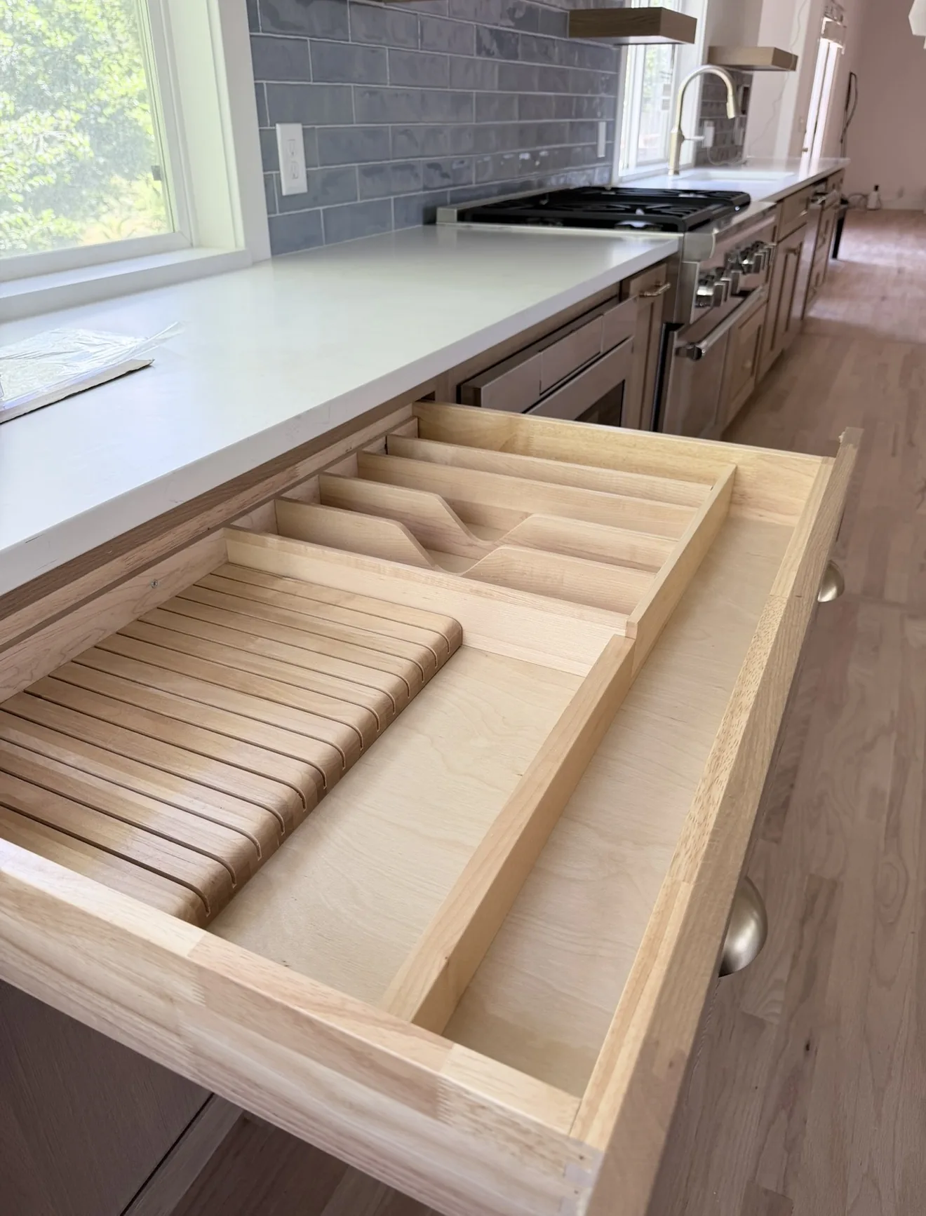 Open oak drawer with a custom knife organizer, blue tile and a stainless range behind it