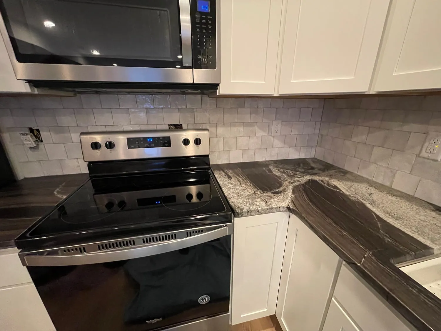 Stainless range with dark leathered-granite counters and gray marble subway backsplash
