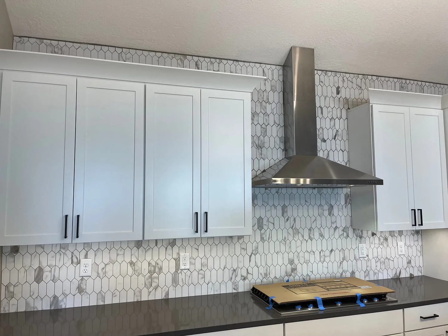 Same kitchen finished range wall: chimney hood, marble mosaic backsplash, black counters
