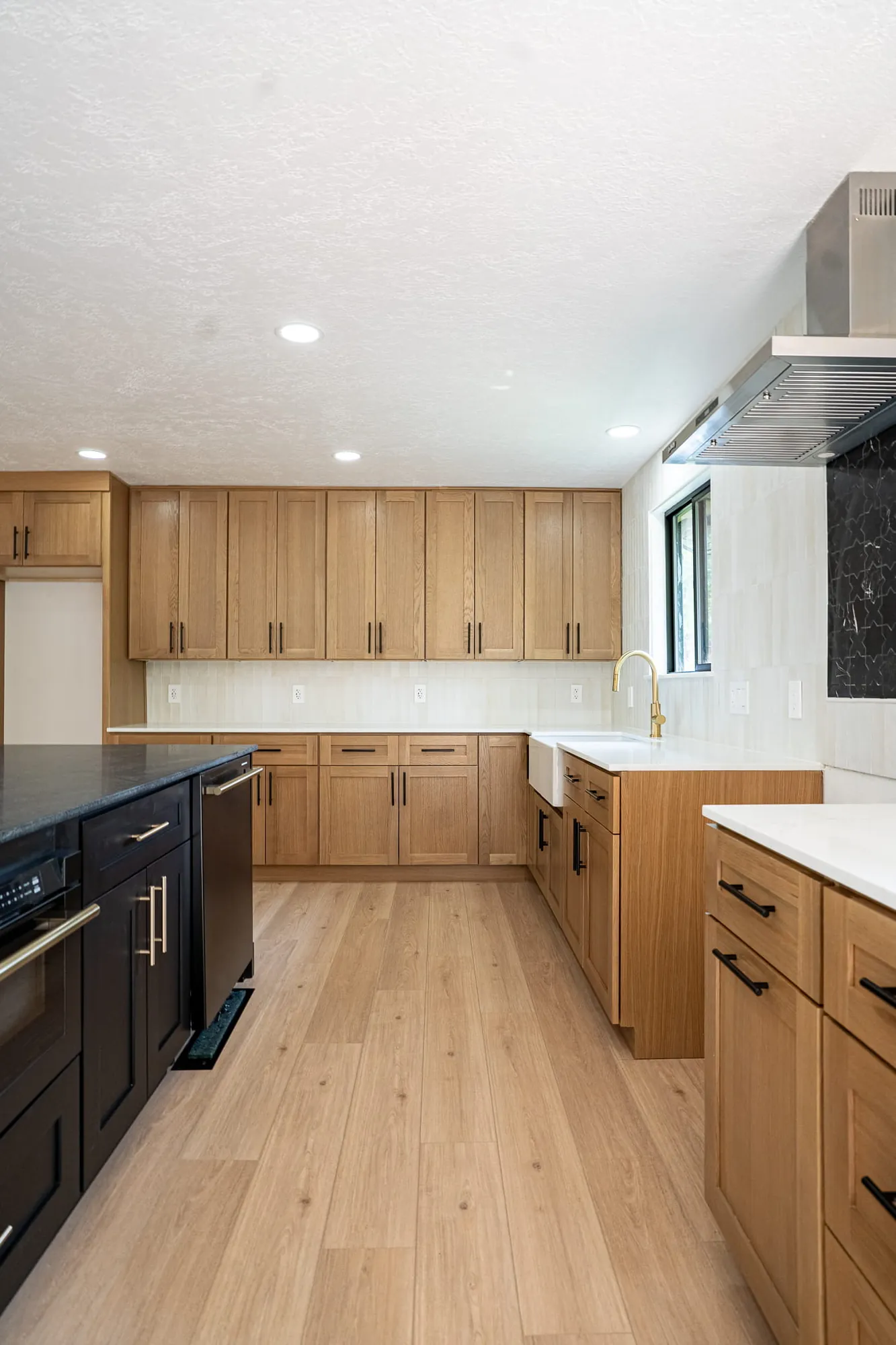 White-oak shaker kitchen with black island, wood-look floor, white quartz