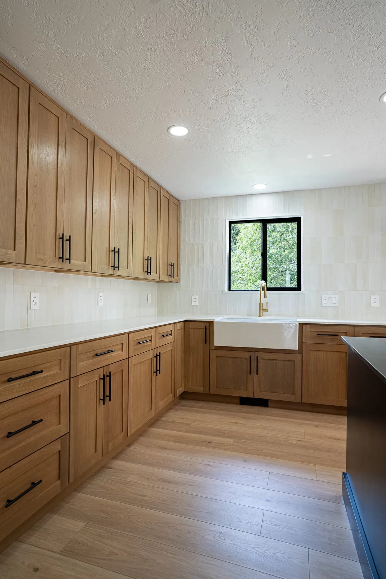 White-oak cabinets wrapping to a black-framed window and farmhouse sink