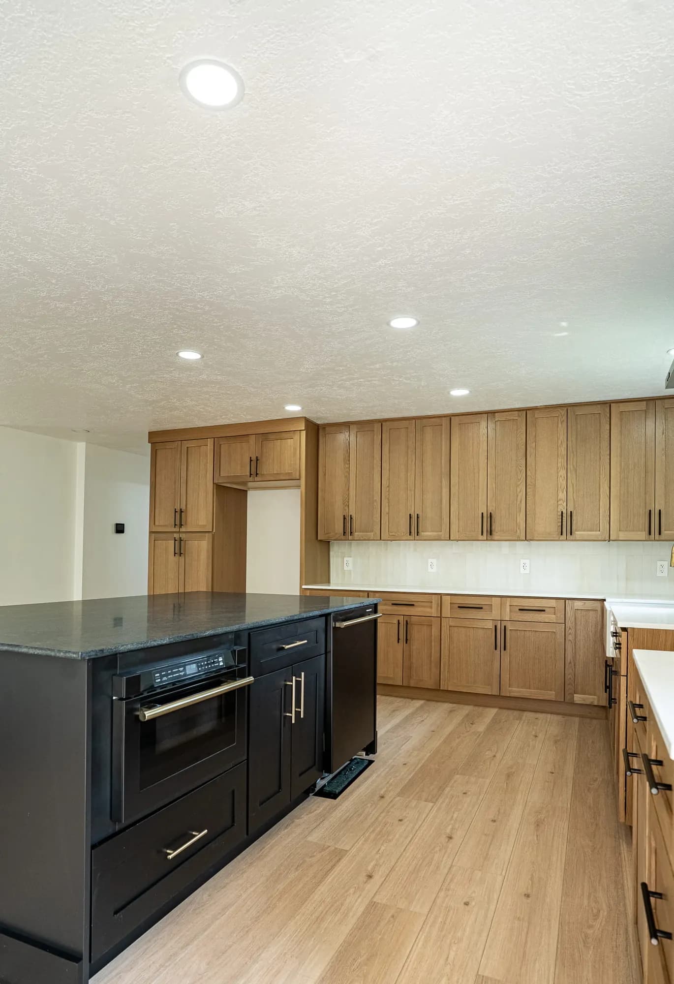 Black island with built-in oven in front of white-oak cabinetry