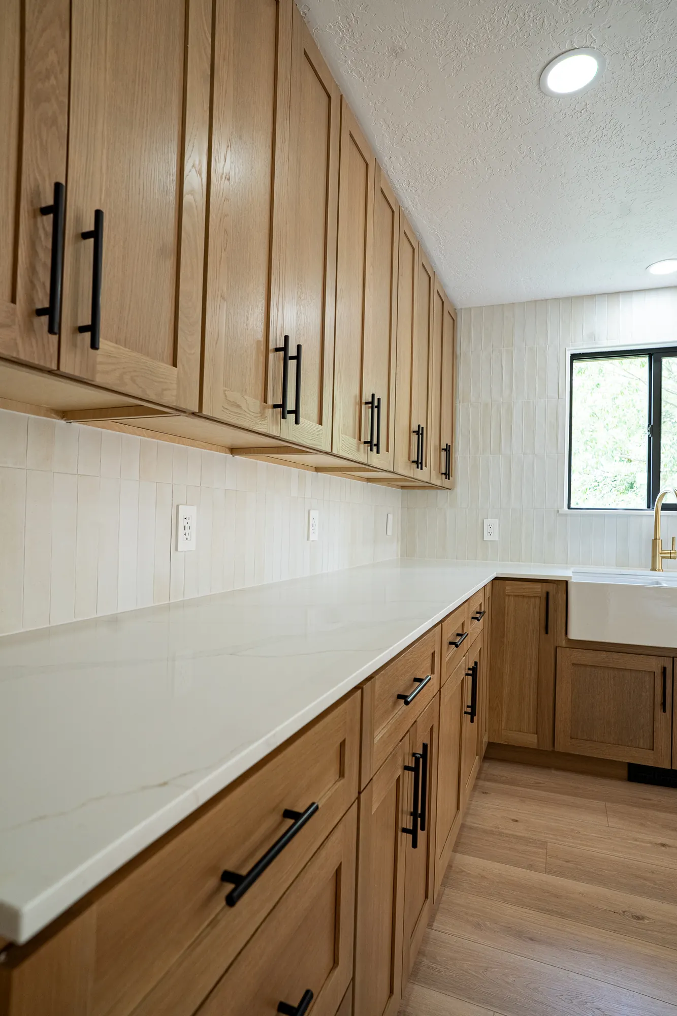 White oak range wall with black pulls, quartz counters, and cream stacked tile