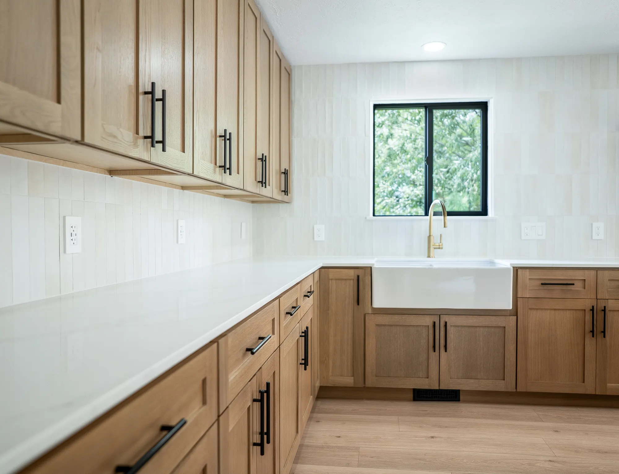 White oak kitchen with an island, farmhouse sink, brass faucet, and cream stacked tile