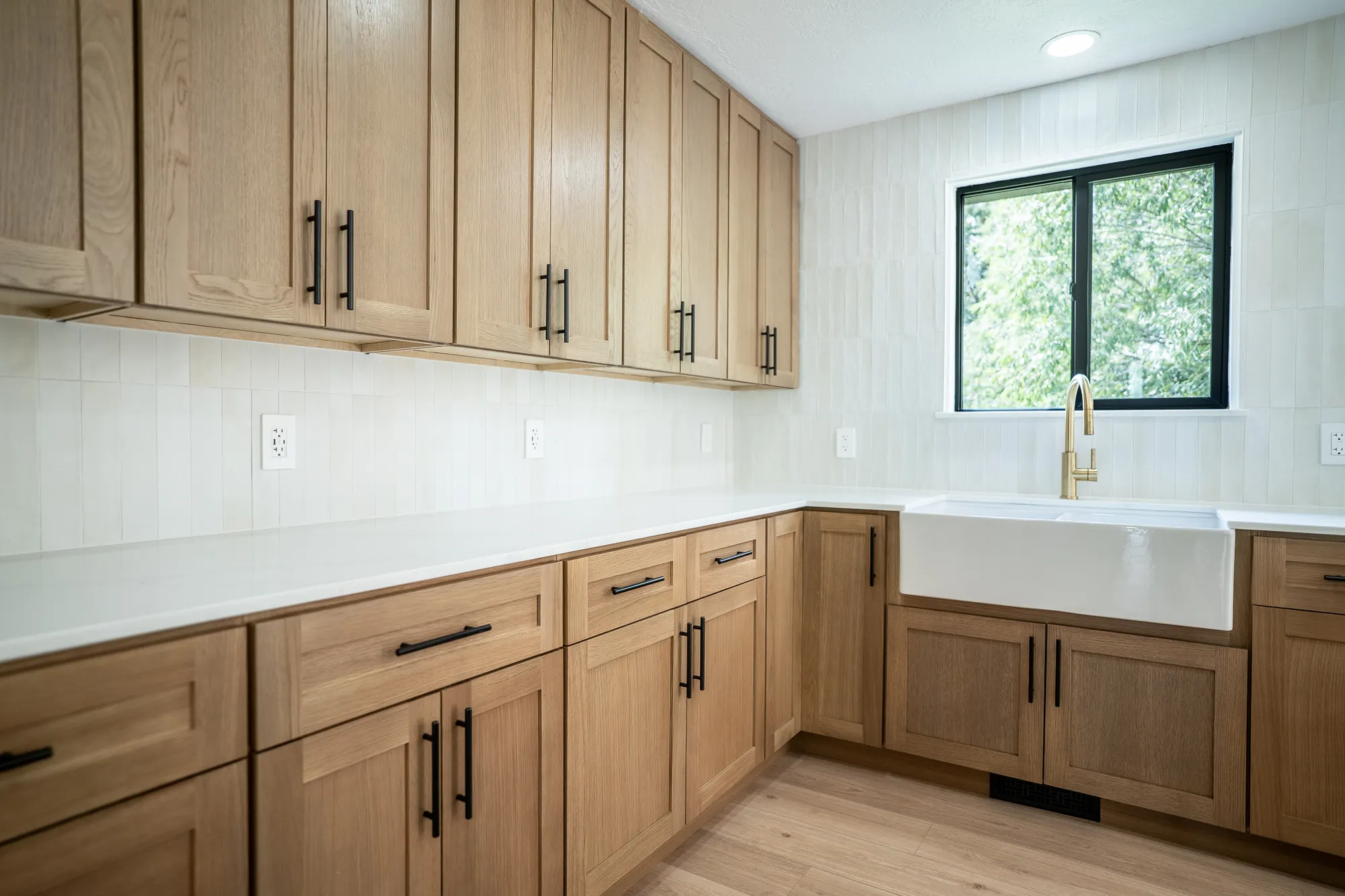 White oak kitchen with black bar stools, a farmhouse sink, and cream stacked tile