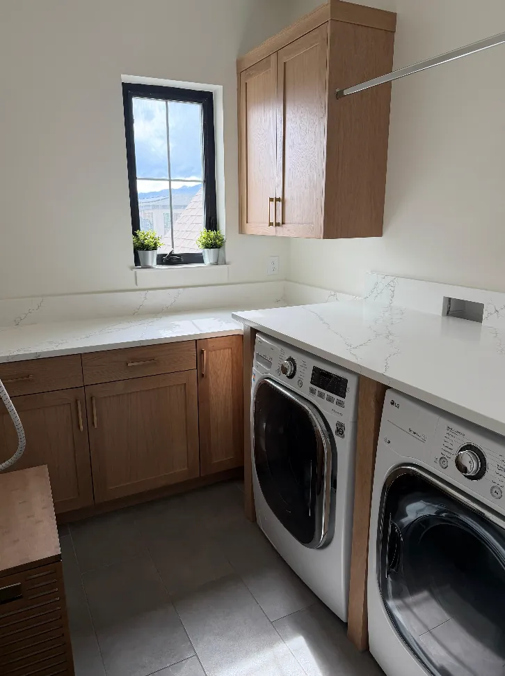 Laundry room: white-oak cabinets, quartz counter, front-load washer and dryer, black window